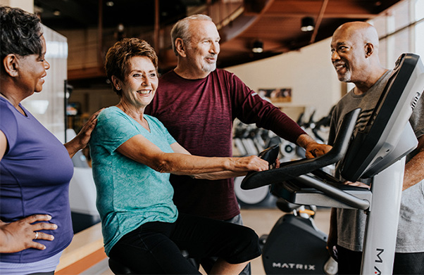Two older couples talking as they work out at the gym.