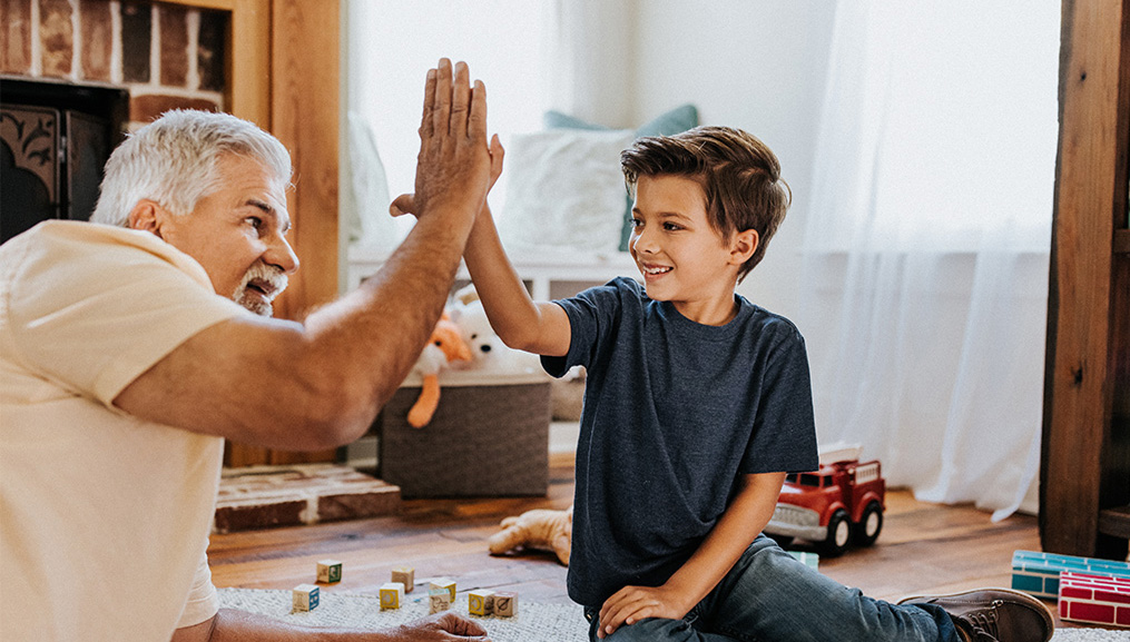 A grandfather high fives his grandson as they play with toys together.