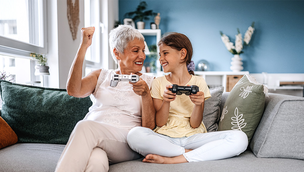 Grandmother and granddaughter playing video games together on the couch.
