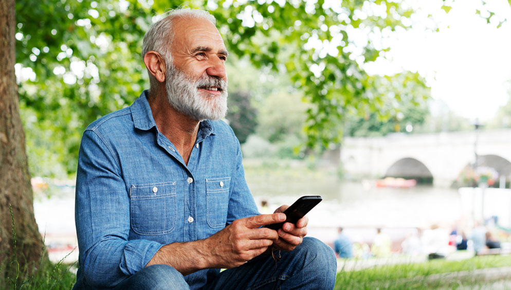 Older man hold cell phone, sitting in nature