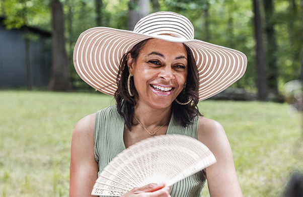 Woman wearing a sun hat and fanning herself with a hand fan.