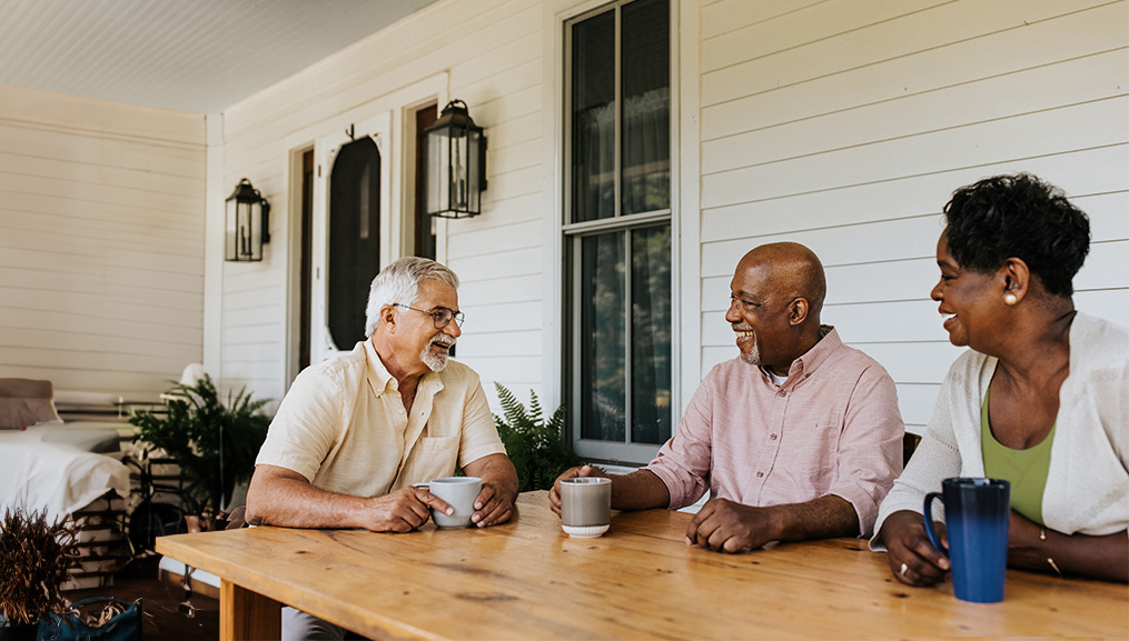 Senior friends enjoying coffee at a porch table.