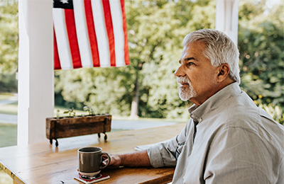 An older man sitting on his front porch with an American flag in the background.