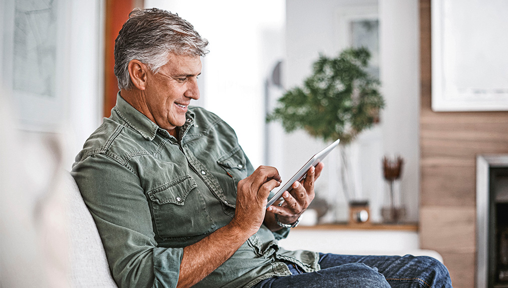  An older man smiling at his tablet as he relaxes on the couch.
