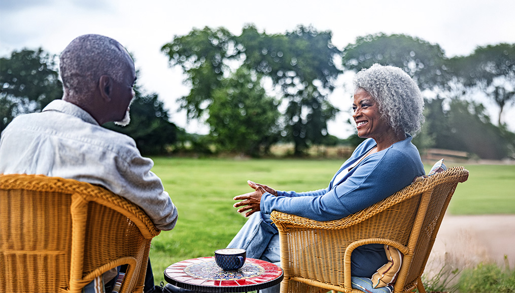 Husband and wife sitting in wicker chairs on their lawn.