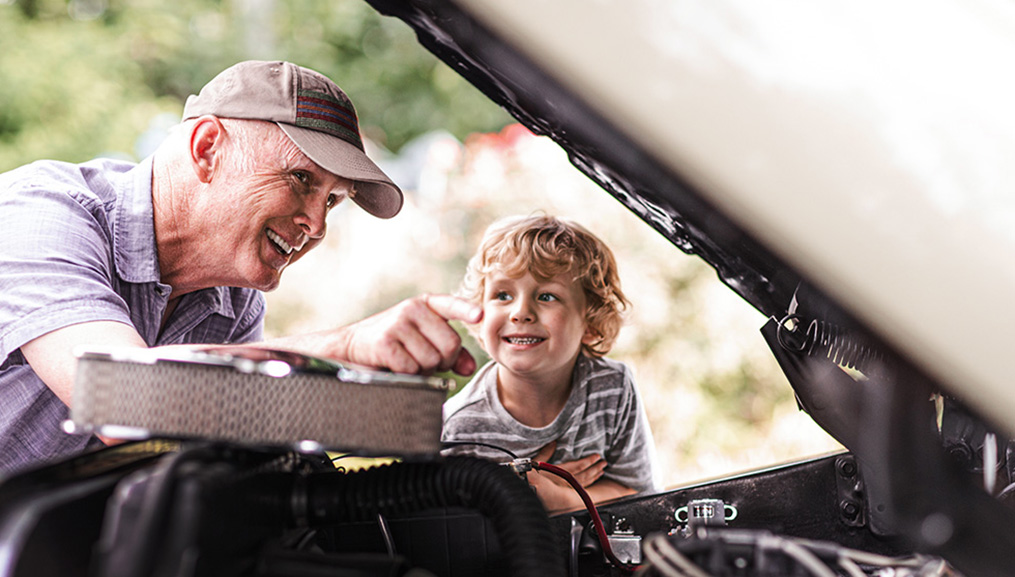 A grandfather working on his car's engine with his grandson.