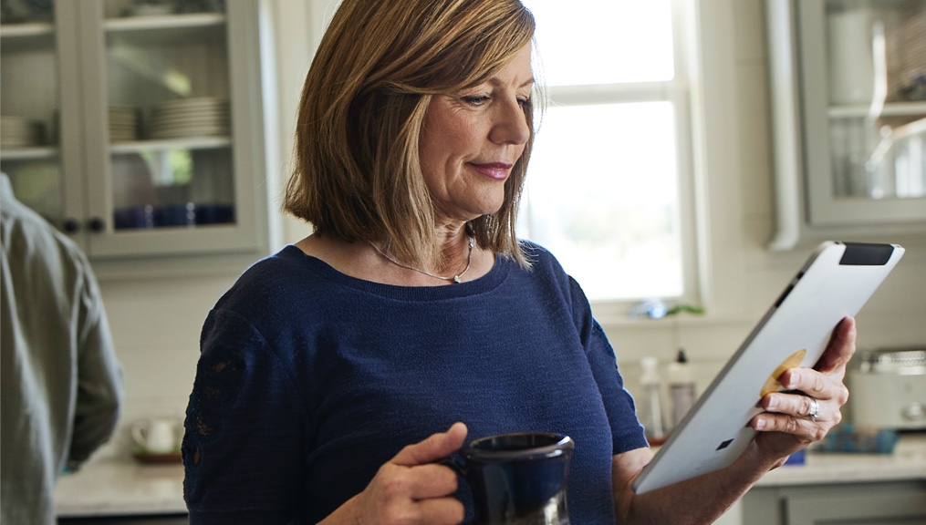Woman drinking coffee and looking at her tablet in the kitchen