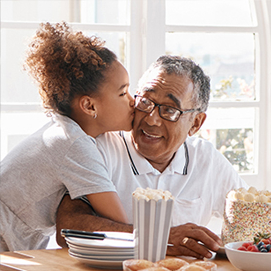 Granddaughter kissing grandfather on the cheek over snacks.