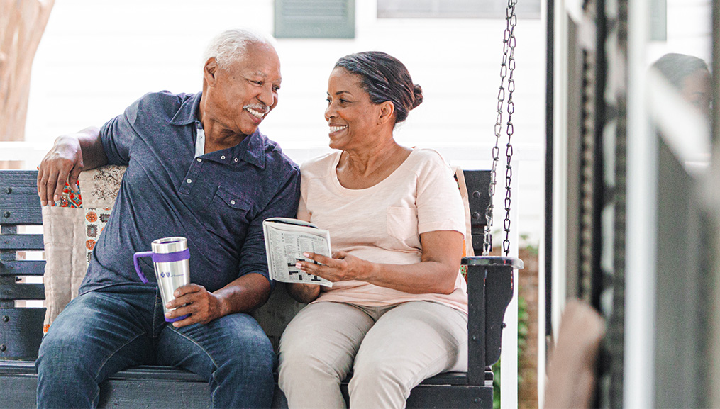 An older couple sitting on their porch swing while they do a crossword puzzle.