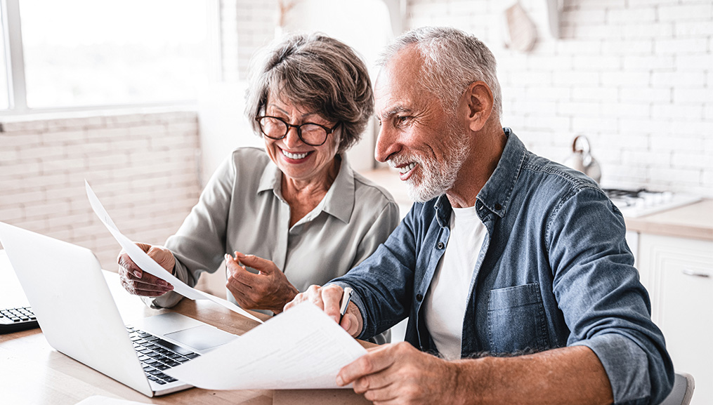 Husband and wife sitting at their kitchen table while shopping on their laptop.